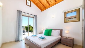 A bedroom with a large bed, a nightstand, a window with a view, and a ceiling with wooden beams.