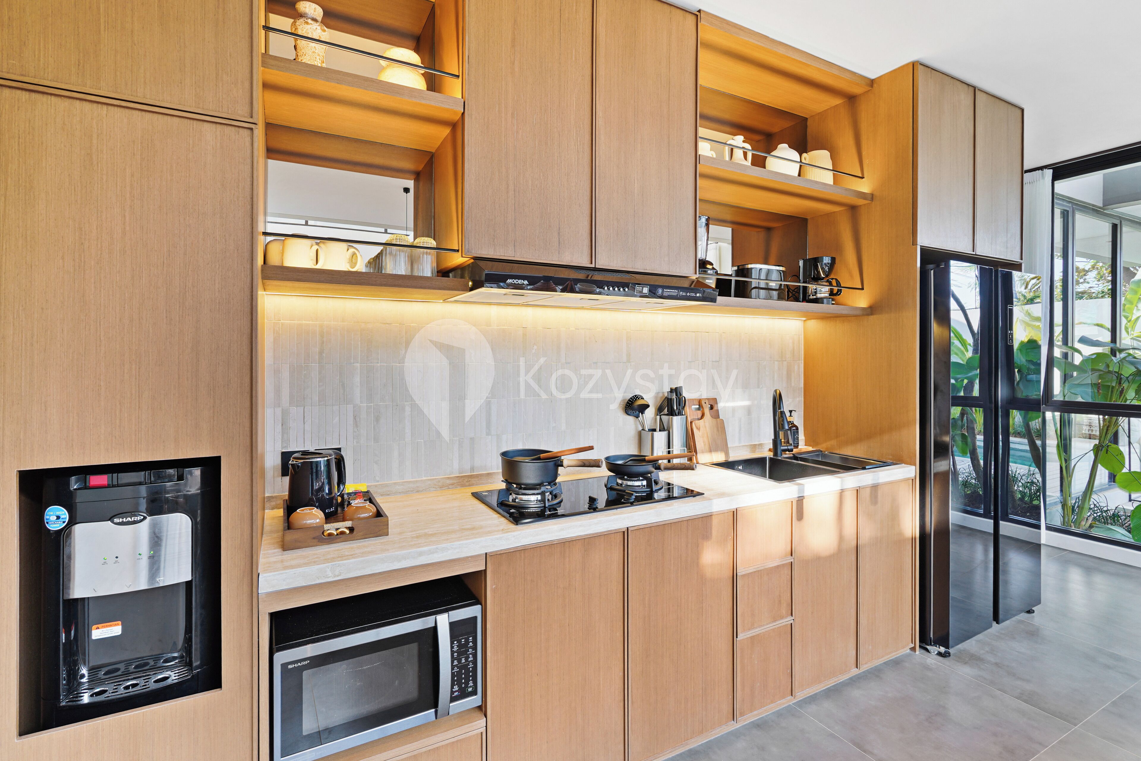 A modern kitchen with built-in appliances, wooden cabinetry, and a large window offering a view of greenery.