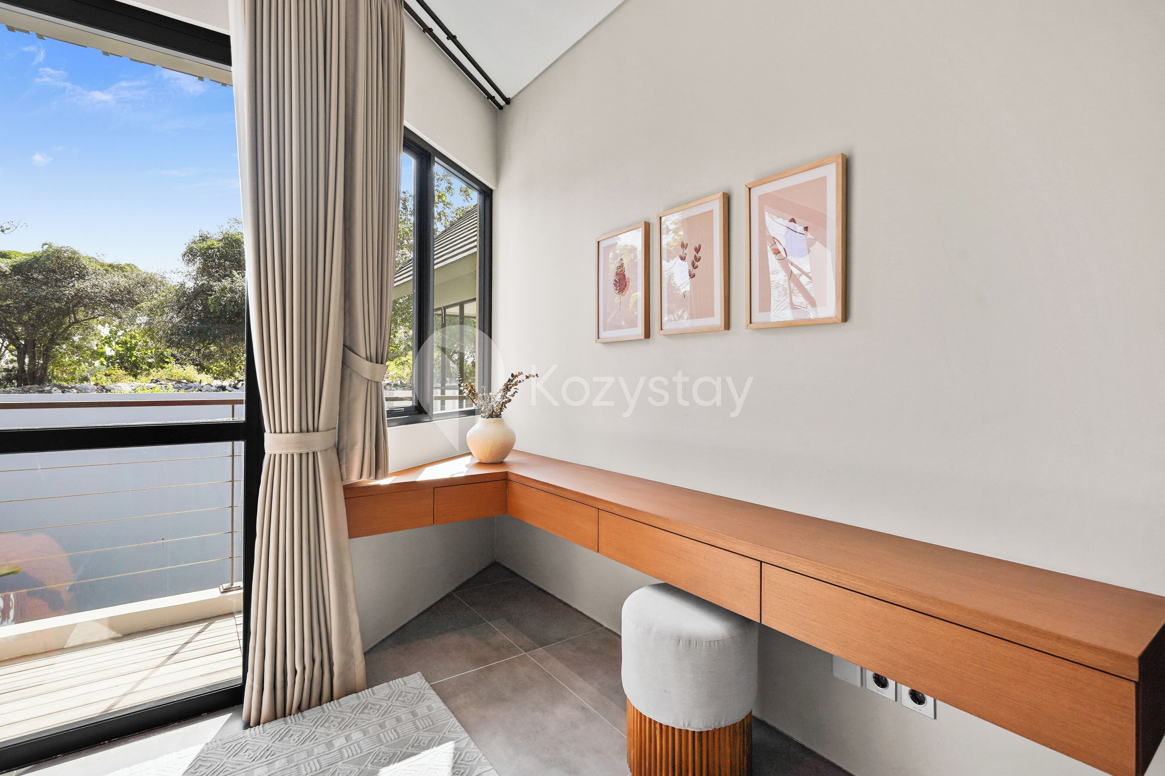 A modern room with a large window, a wooden desk, and three framed pictures on the wall.
