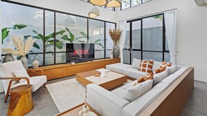 Een moderne woonkamer met een grote televisie, comfortabele zitplaatsen en grote ramen.