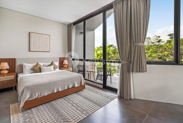 Un dormitorio moderno con una cama grande, una mesita de noche, una lámpara de pared y vistas a un balcón con mobiliario exterior.