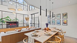 Een moderne eetruimte met een lange houten tafel gedekt voor zes personen, omringd door rieten stoelen. Een groot raam biedt uitzicht op groen buiten.