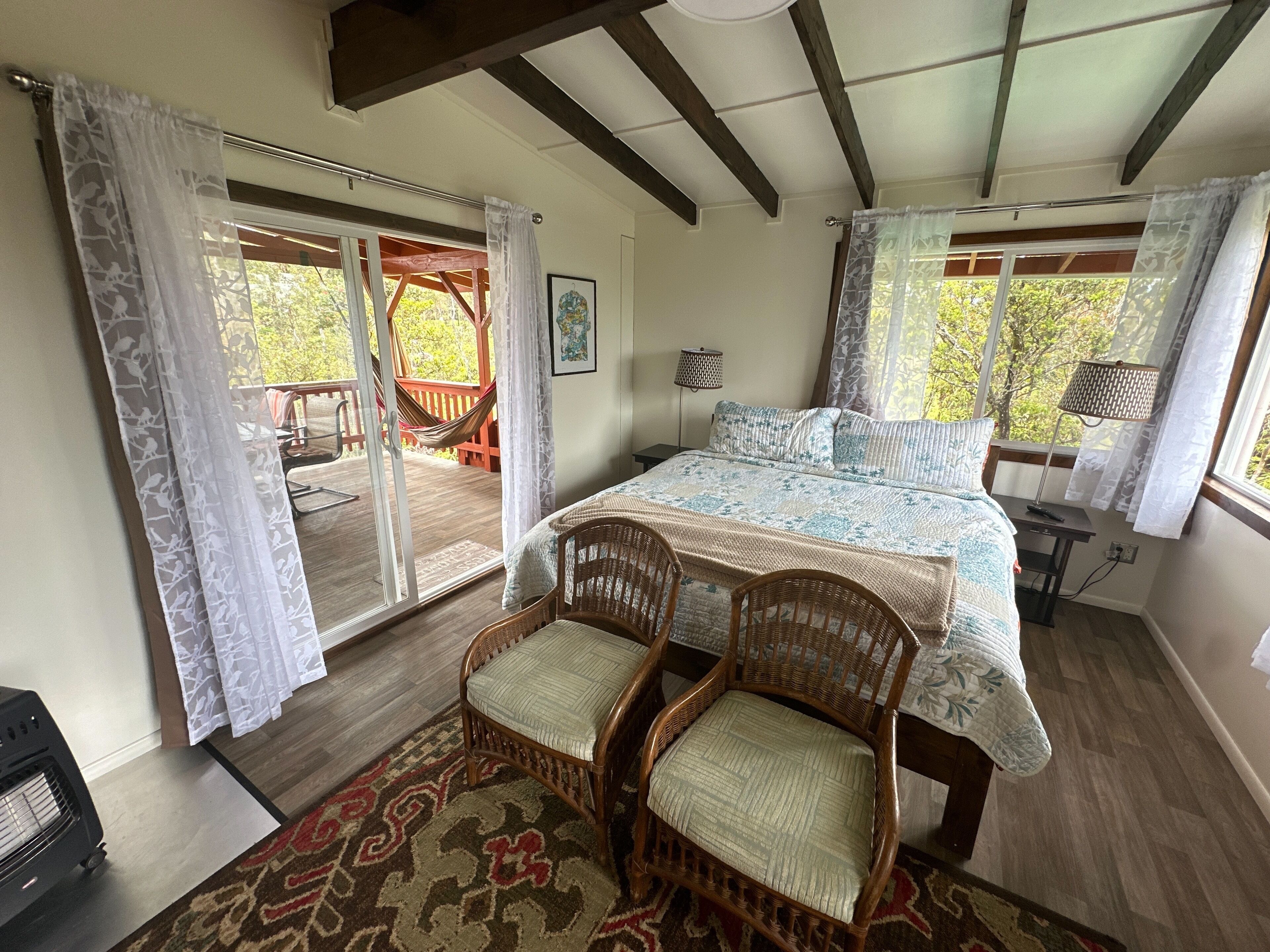 Une chambre à coucher avec un lit, deux fauteuils en osier, un bureau en bois et une vue sur l’extérieur.