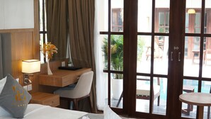 A hotel room with a bed, a desk, a chair, a lamp, and a view of the outside.