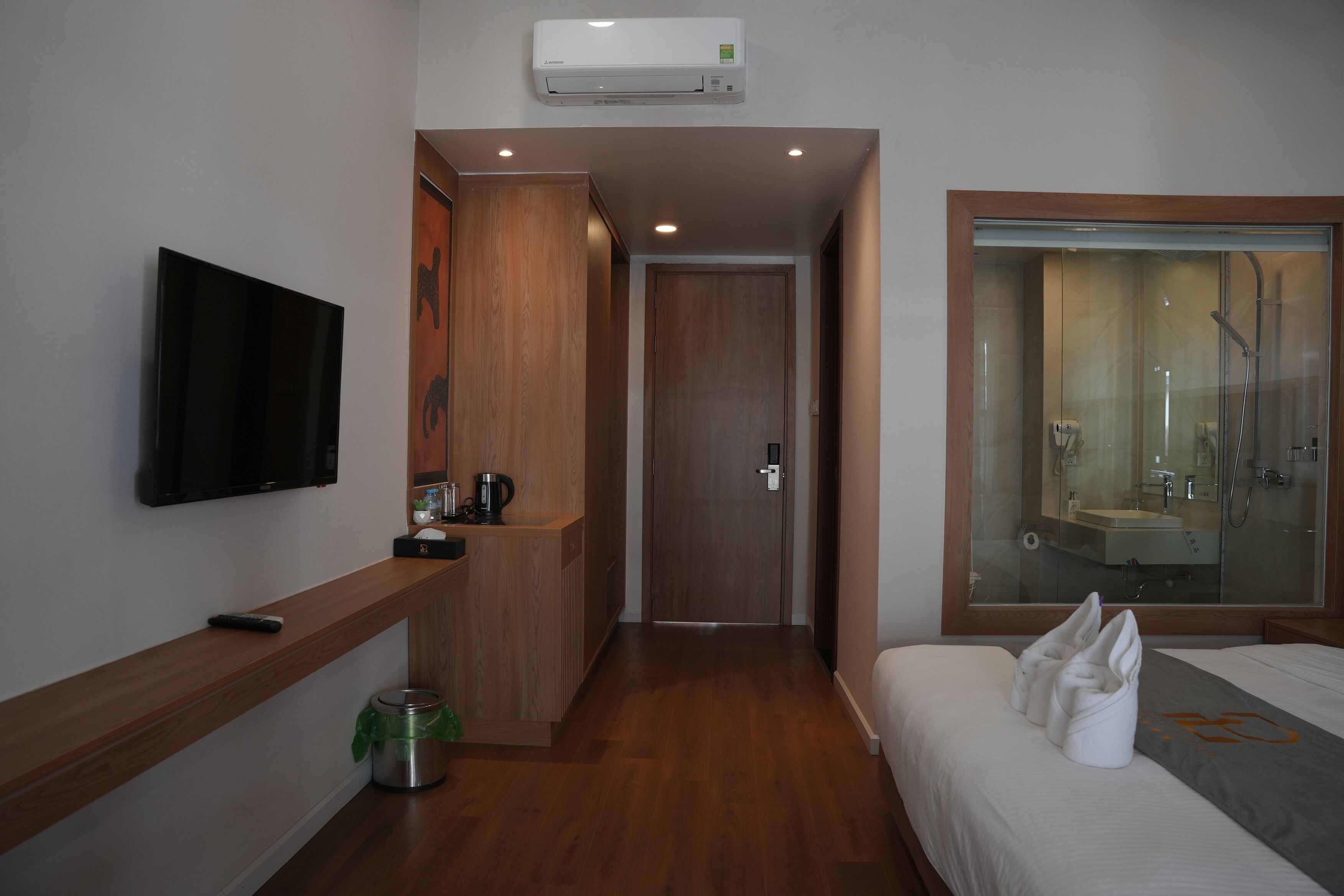A hotel room with a flat-screen TV, a wooden cabinet, a minibar, a shower area, and a bed with towels.