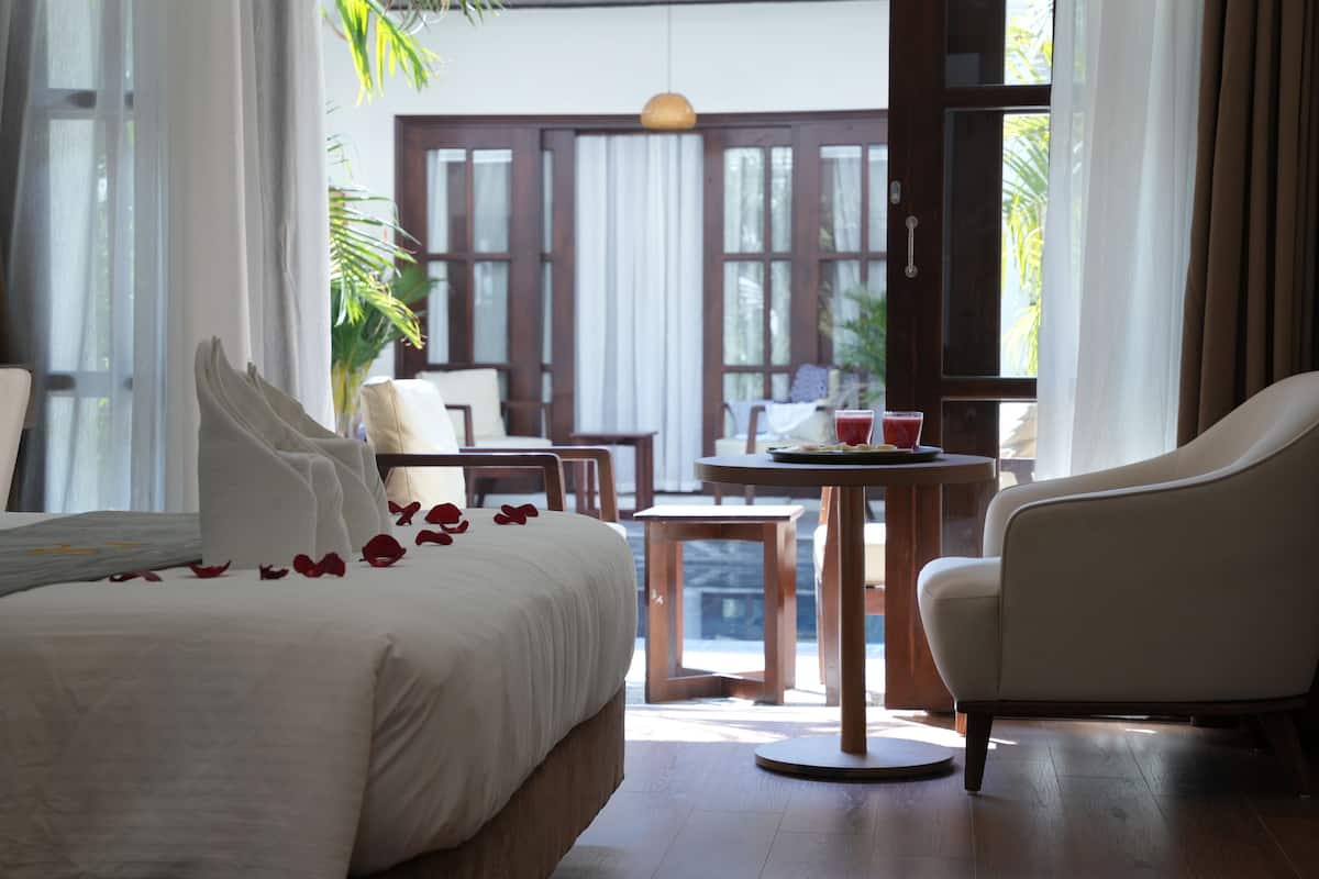A hotel room with a bed, a chair, a table, and a view of the outside.