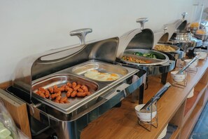 Un bufé con diversas opciones de comida, incluyendo salchichas, huevos y verduras.