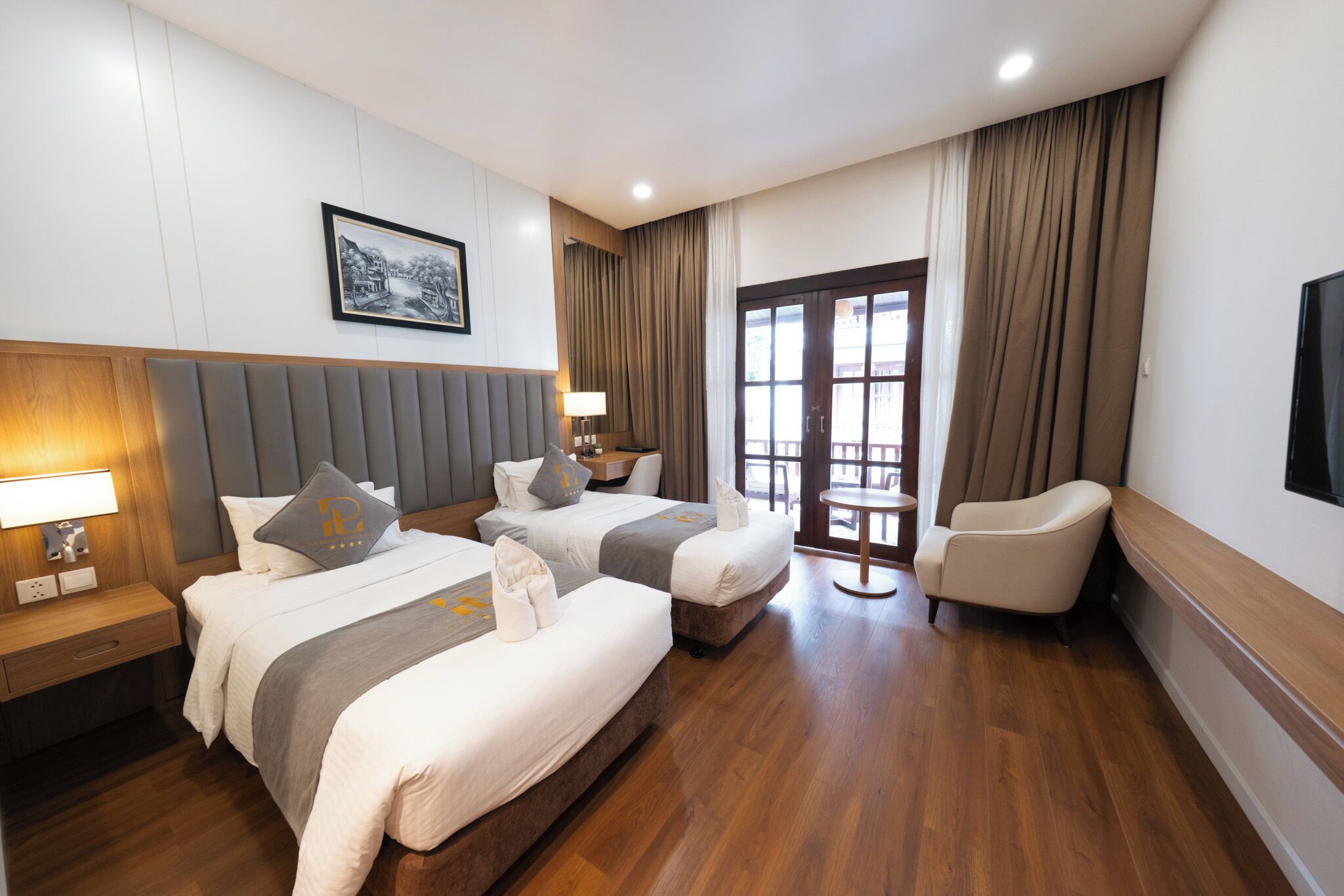 A hotel room with two beds, a desk, a chair, a TV, and a large window with curtains.