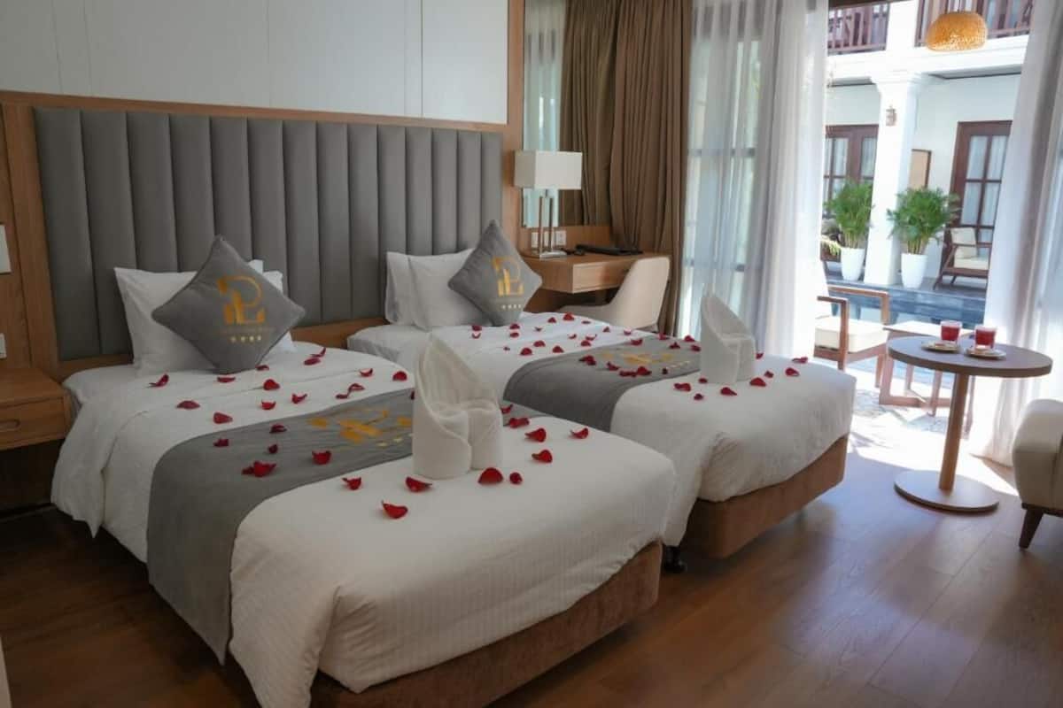 A hotel room with two beds, a desk, and a balcony with plants.