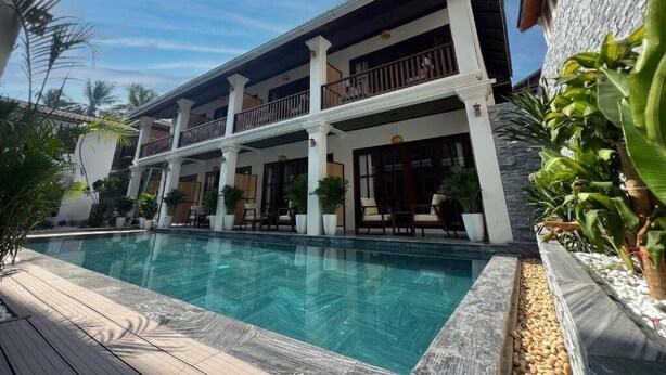 A two-story building with a swimming pool, outdoor seating, and a stone wall.