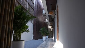 A narrow corridor with tiled flooring, large potted plants, and a bamboo wall.