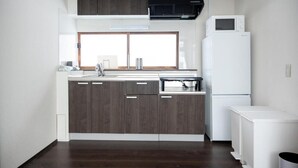 A modern kitchen with dark wood cabinets, a white refrigerator, and a microwave on top. - BIEI RELAX STAY A (Biei)