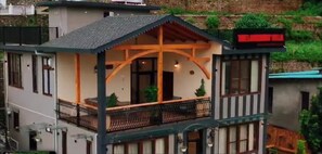 A two-story house with a balcony, a wooden porch, and a red sign on the roof. - The Lakemont Villa (Harinagar Chanddeva)