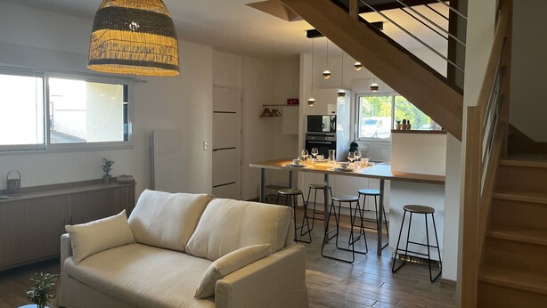 Una sala moderna con un sofá, un comedor con taburetes y una cocina con una isla central.