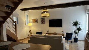 Una sala de estar moderna con un sofá, una mesa de comedor, una lámpara, un televisor y una escalera.