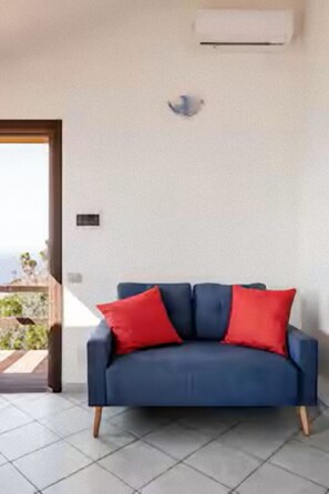 A room with a blue sofa, red cushions, a tiled floor, and a door leading outside. - Villa Sunny Side - Panoramic View (Trinità d'Agultu e Vignola)