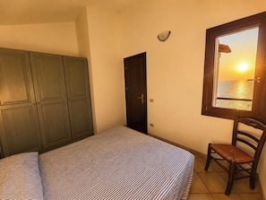 Un dormitorio con cama, una silla, un armario, una puerta y una ventana con vista al mar.