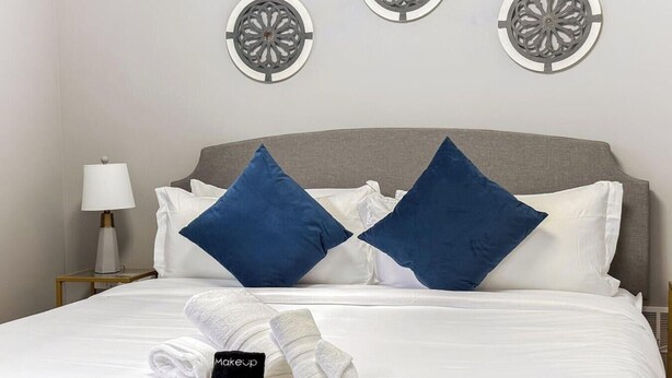 A neatly made bed with white linens, two blue pillows, and a folded towel with a black tag.
