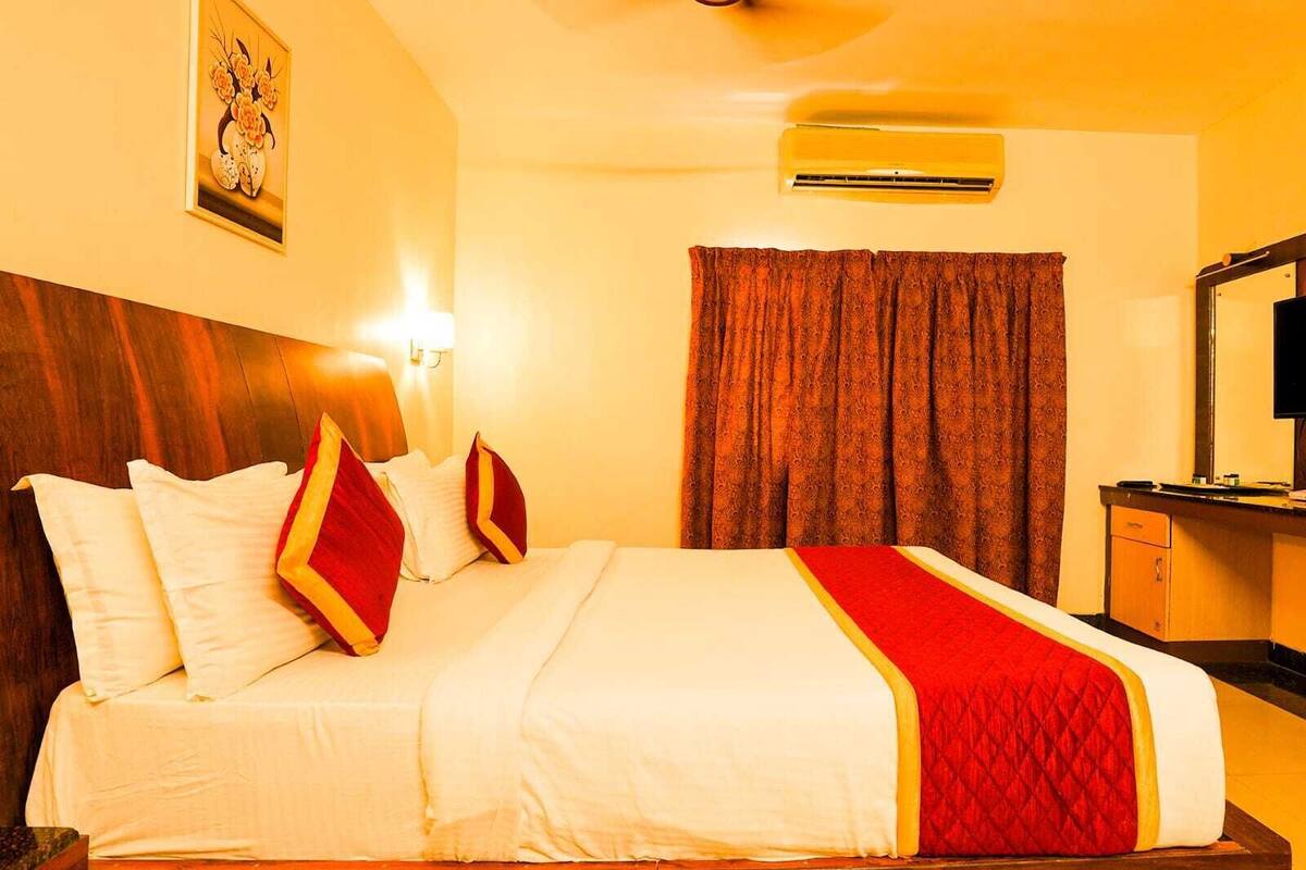 Habitación de hotel con una cama grande, cabecera de madera, mesita de noche, un espejo y aire acondicionado instalado en la pared.
