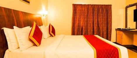A hotel room with a large bed, a wooden headboard, a bedside table, a mirror, and a wall-mounted air conditioner.