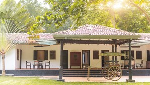A building with a tiled roof, a covered porch with chairs, a wooden cart, and a palm tree. - Villa Wild Ceylon by TSC (NW)
