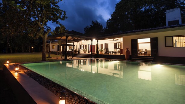 A swimming pool with a covered patio area, a well-lit entrance, and a view of the surrounding trees. - Villa Wild Ceylon by TSC (NW)