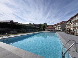 Une piscine à l’eau claire, sous un ciel dégagé, entourée d’immeubles dotés de balcons.