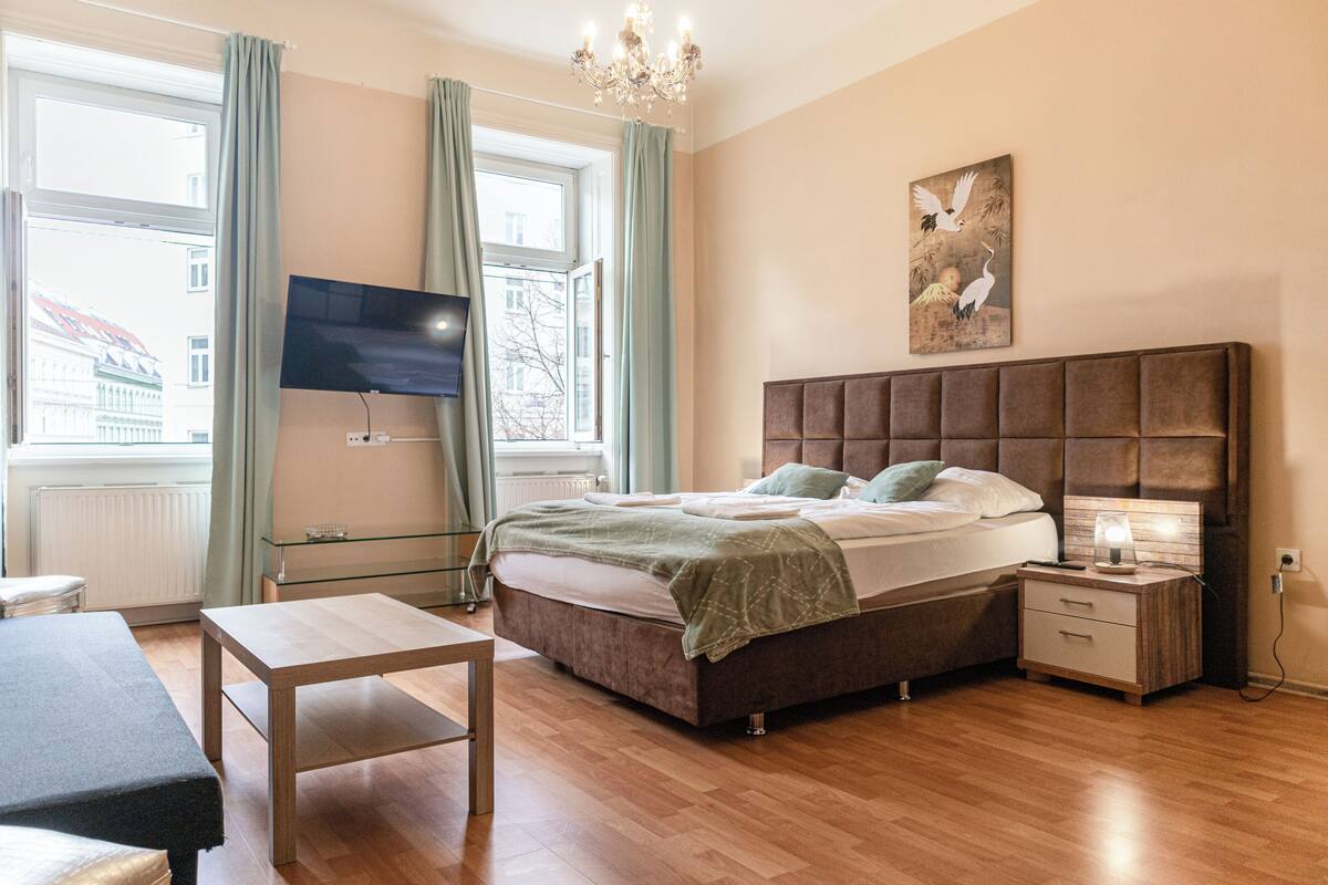 A bedroom with a large bed, bedside table, nightstand, and a TV mounted on the wall.