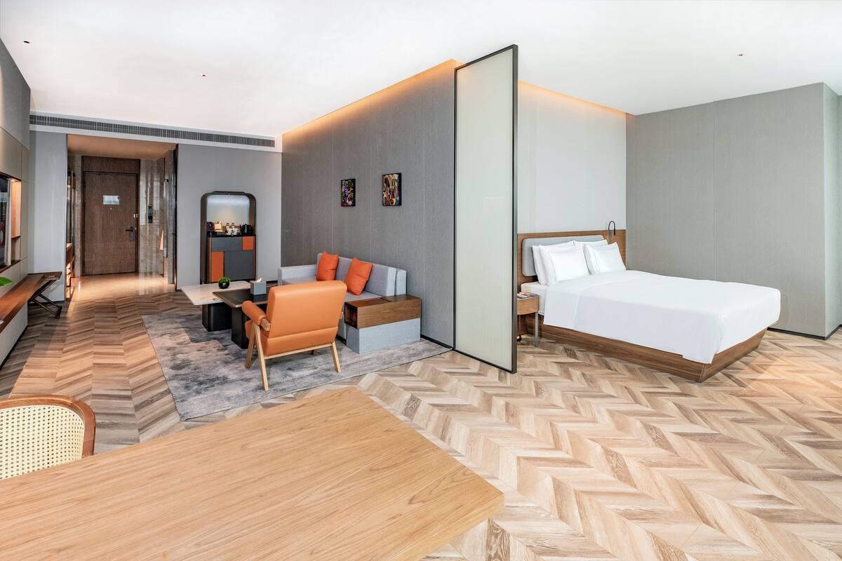 Ein modernes Hotelzimmer mit einem großen Bett, einer Couch, einem Esstisch und einer kleinen Küchenzeile.