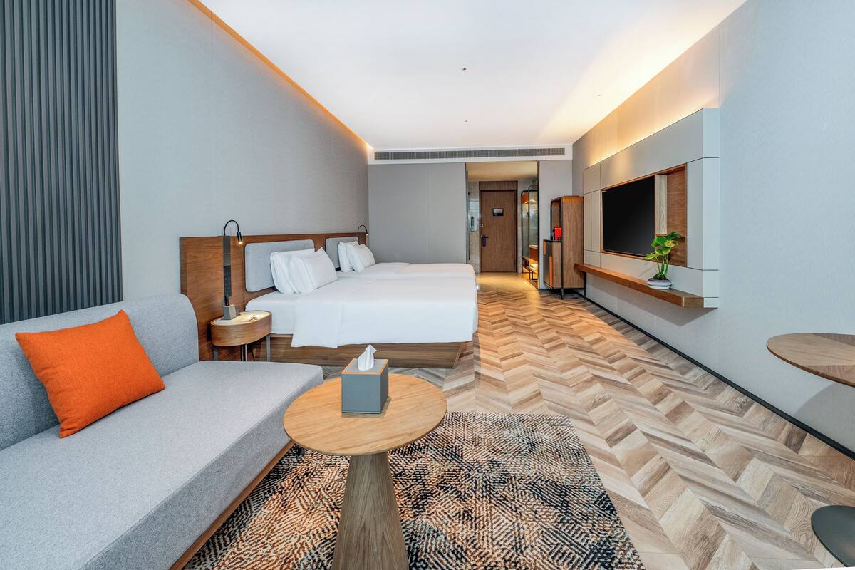 Ein Hotelzimmer mit Bett, Sofa, einem kleinen Tisch, Fernseher und Spiegel.