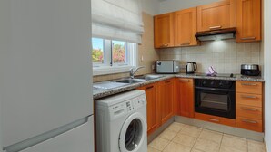 Een keuken met een Bosch wasmachine, een magnetron, een koffiezetapparaat en houten keukenkastjes.