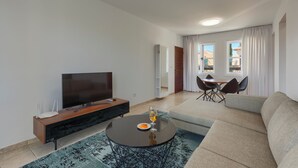 Een moderne woonkamer met een flatscreen televisie, een salontafel met een glas wijn, een bank en een eethoek met stoelen en een tafel.