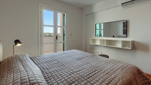 Een slaapkamer met een bed, een bureau, een stoel, een lamp, een spiegel en een raam.