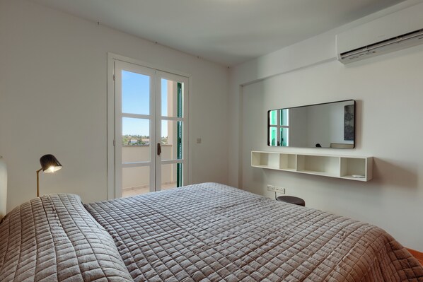Une chambre à coucher avec un lit, un bureau, une chaise, une lampe, un miroir et une fenêtre.