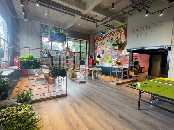 Un intérieur moderne avec une table de ping-pong, une fresque murale et une enseigne sur laquelle on peut lire « PALOQUEMAO ».