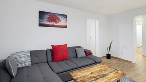 Un salon moderne avec un canapé d’angle gris, une table basse en bois et un coussin rouge.