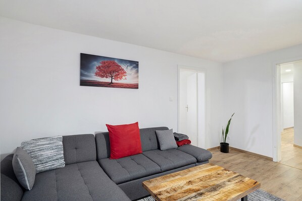 A modern living room with a grey sectional sofa, a wooden coffee table, and a red pillow.