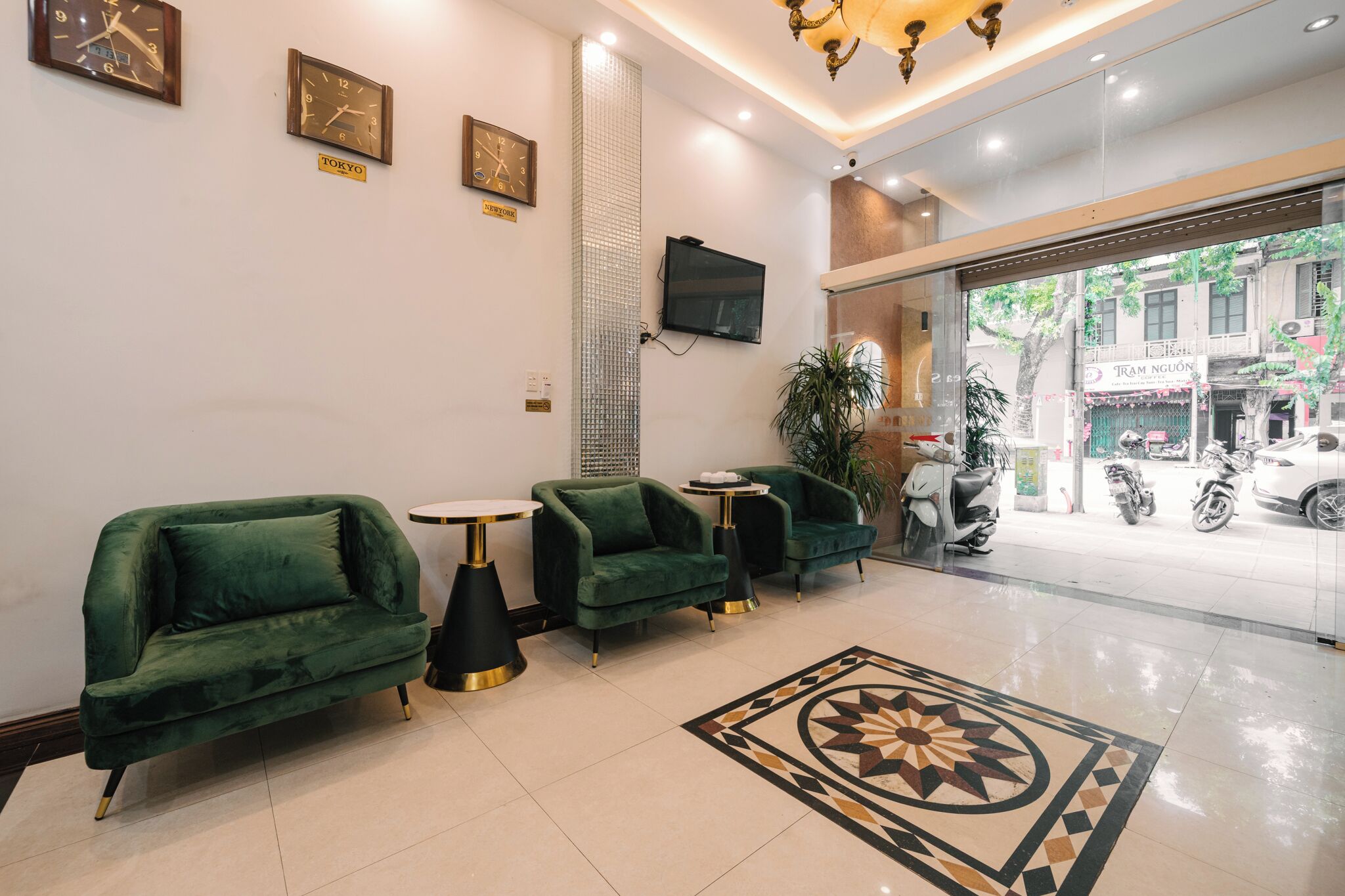A lobby with green upholstered chairs, a small round table, a decorative rug, and a television mounted on the wall.
