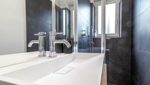 Une salle de bain moderne avec un grand lavabo blanc, des robinets chromés et des murs recouverts de carreaux foncés.