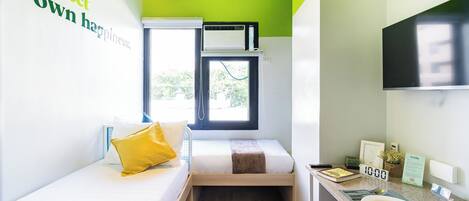 A compact room with a bed, a small desk, a window, and a mounted TV.