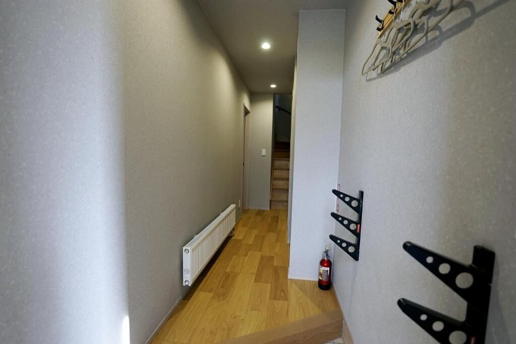 A narrow hallway with wooden flooring and a radiator on the left. There is a fire extinguisher on the right wall.