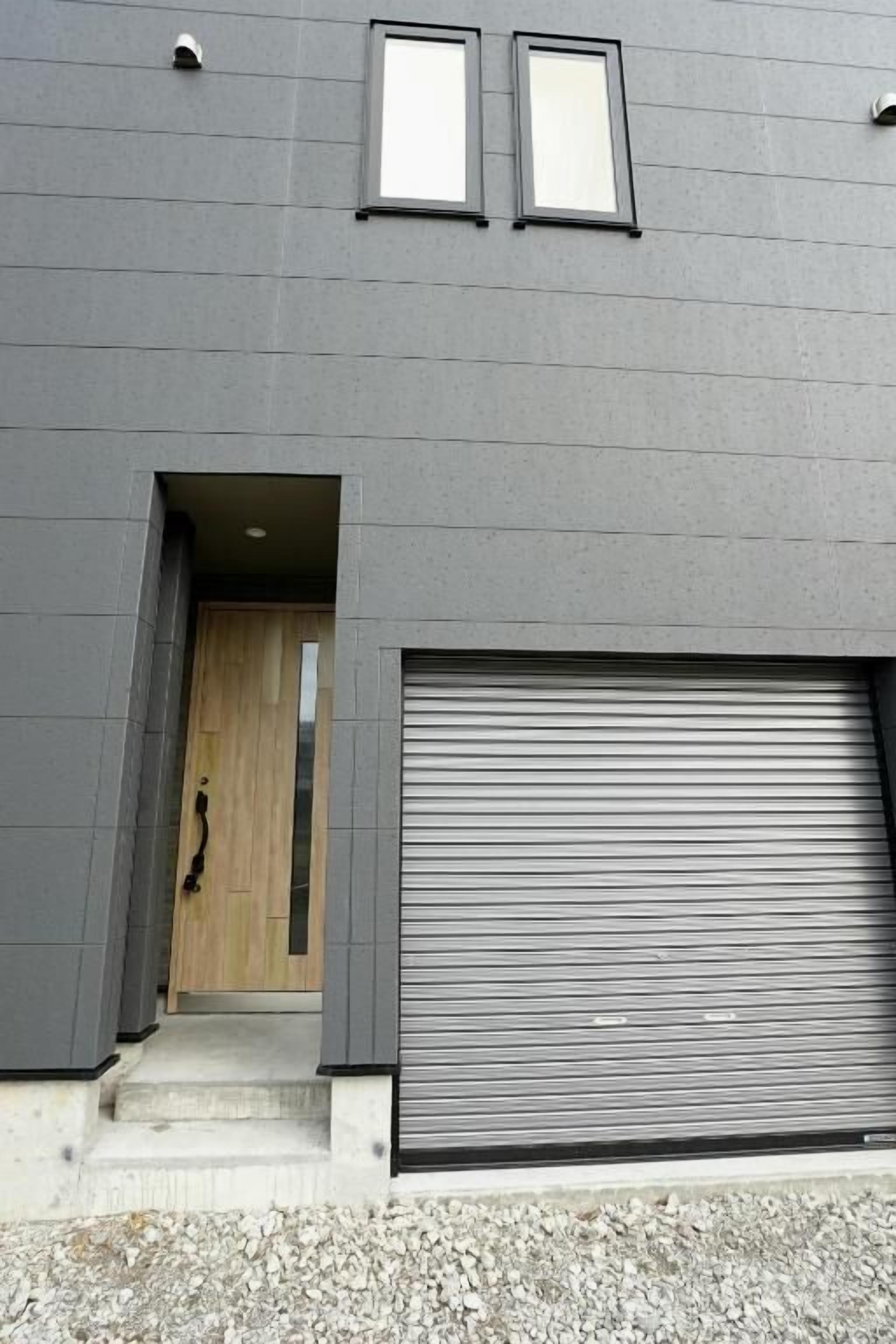 A modern building with a grey facade, a wooden door, and a large garage door.