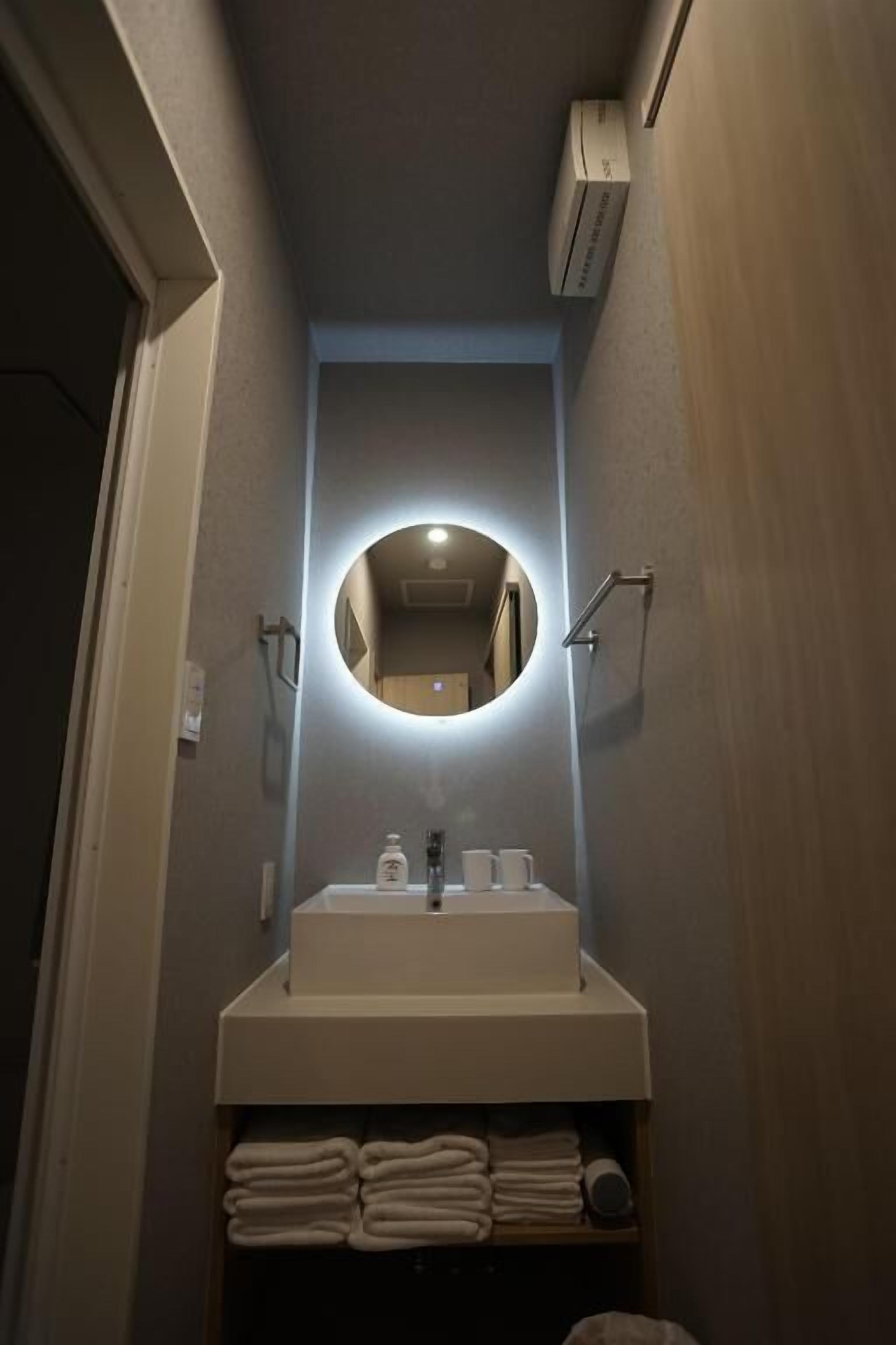 A narrow bathroom with a round mirror, a sink, and a towel rack.