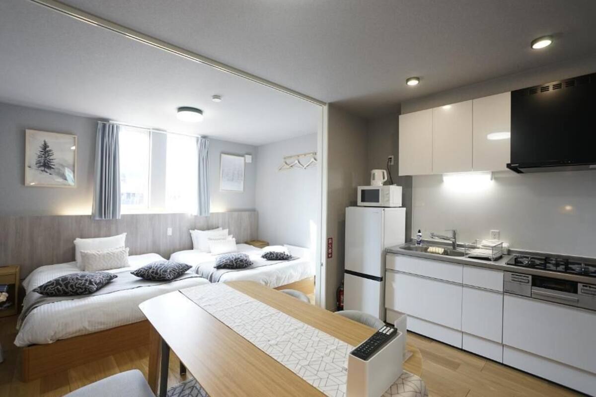 Une chambre d’hôtel moderne avec deux lits, une table à manger, un coin cuisine et une grande fenêtre.