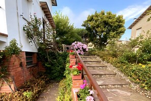 Un escalier en pierre avec une rampe métallique, entouré de verdure et de plantes en fleurs.