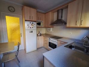 A kitchen with wooden cabinets, a refrigerator, a microwave, an oven, and a sink.