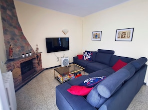 A living room with a blue sofa, a fireplace, a flat-screen TV, and framed artwork on the wall.