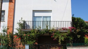 Una casa de dos pisos con un balcón, un muro de piedra y una reja metálica.