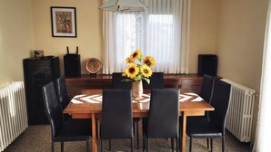 Un comedor con una mesa de madera, sillas negras, un jarrón con girasoles, un cuadro enmarcado y un radiador.