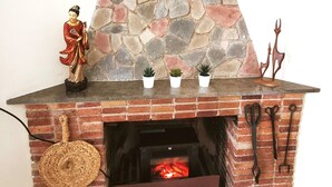 Una chimenea de ladrillo con repisa de piedra, una estatua decorativa y tres pequeñas macetas con plantas.